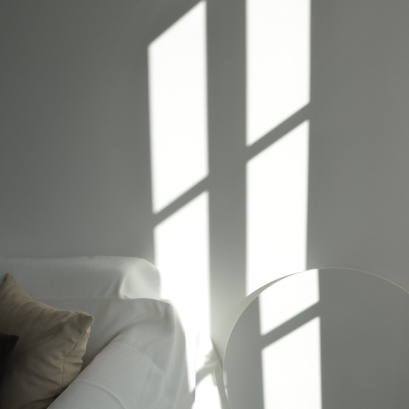 Helle Schatten von Fenstern auf einer weißen Wand und einem Sofa mit Kissen.