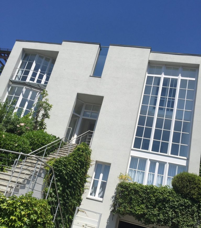 Modern Gebäude mit großen Fenstern, umgeben von Grün und einer Treppe.