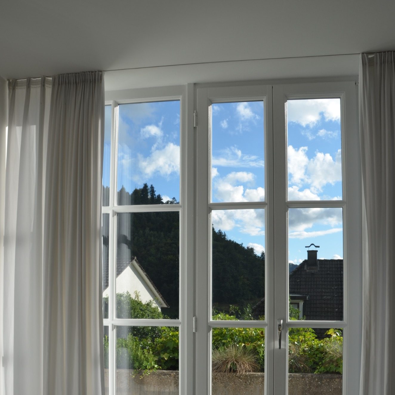 Blick aus einem Fenster mit blauen Himmel, Wolken und grüner Landschaft.
