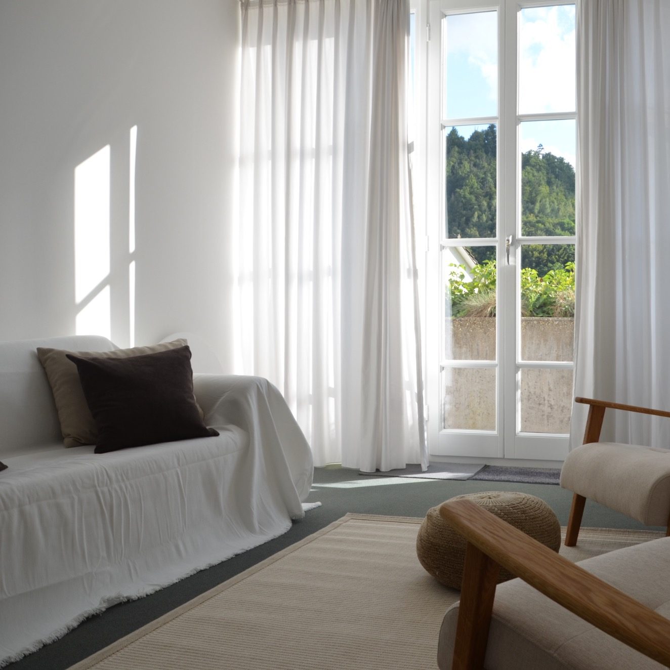 Helles Wohnzimmer mit einem Sofa, Stühlen und großen Fenstern, die Tageslicht hereinlassen.